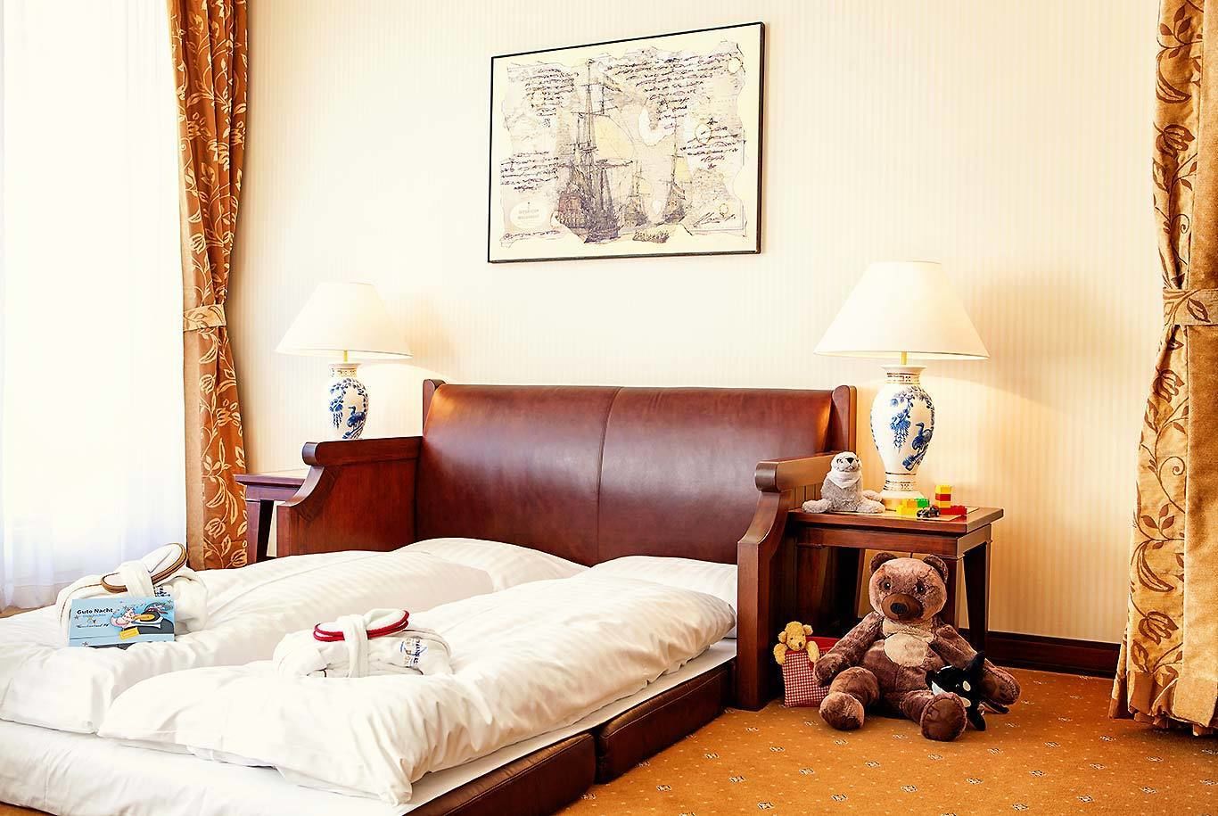 Una habitación de hotel con una cama grande, dos mesitas de noche con lámparas, un osito de peluche y un cuadro en la pared.