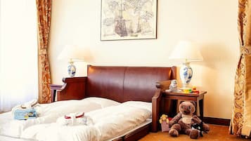 Une chambre d’hôtel avec un grand lit, deux tables de chevet avec des lampes, un ours en peluche et une œuvre d’art encadrée accrochée au mur.