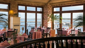 Ein Restaurant mit karierten Tischdecken, Holzkufen und großen Fenstern mit Blick auf ein Gewässer.