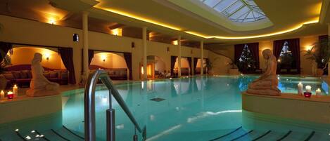 An indoor swimming pool with a skylight, a sunken seating area, and a statue.