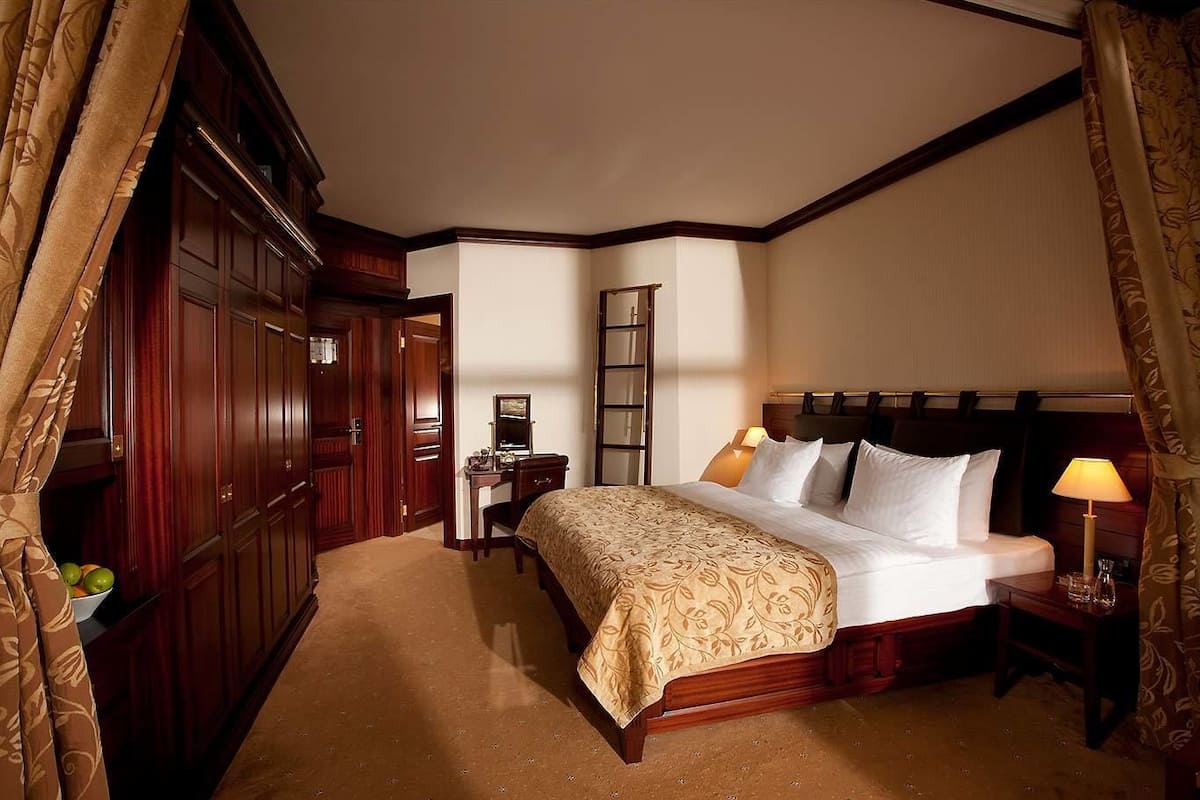 Ein Hotelzimmer mit einem großen Bett, einem Schreibtisch mit Stuhl, einem Kleiderschrank und einem Nachttisch mit Lampe.