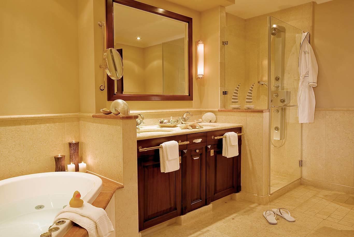 A bathroom with a bathtub, a vanity with a mirror, a shower, and a pair of slippers on the floor.