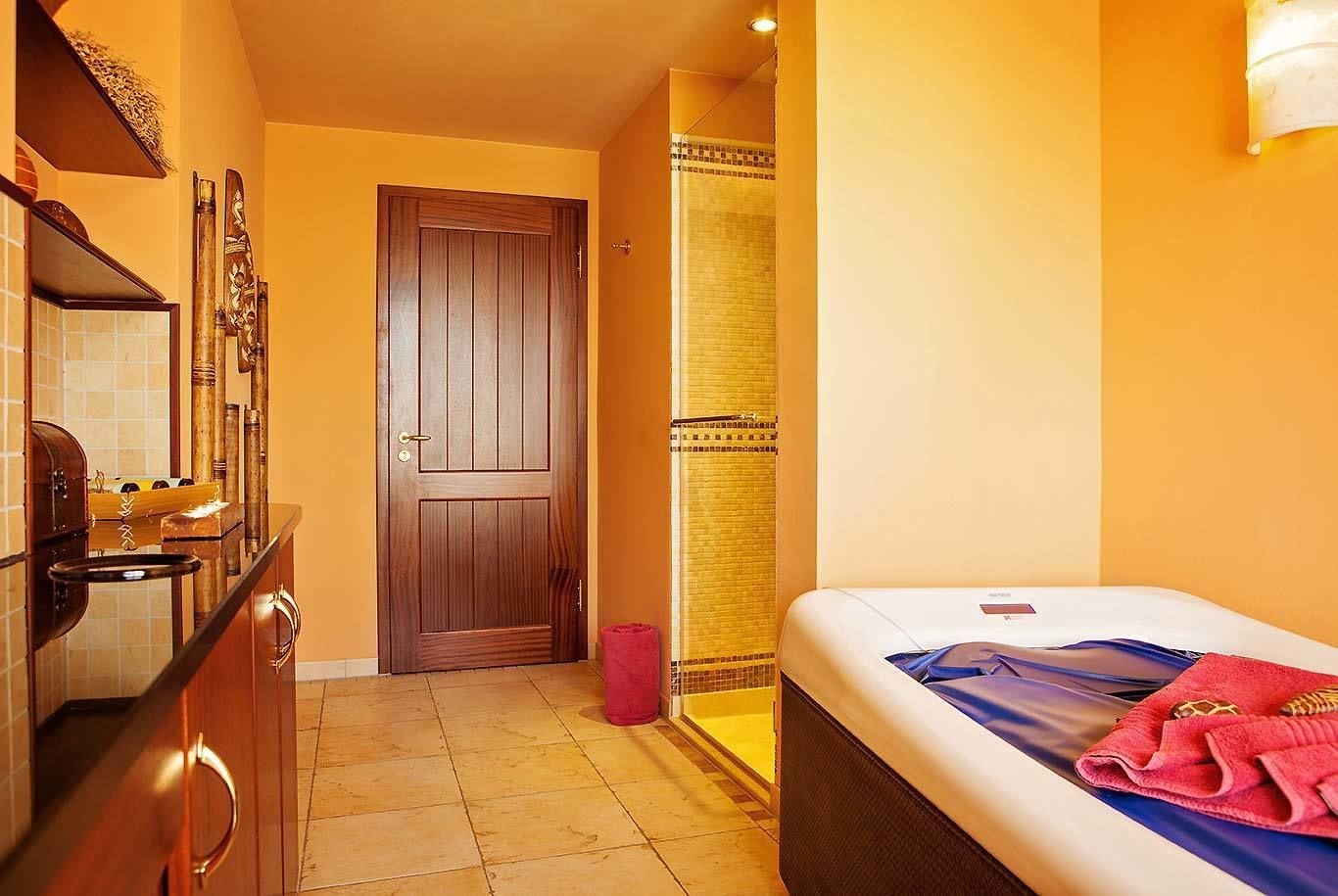 Ein Hotelzimmer mit Holztür, Badezimmer mit Dusche und Bett mit blauer und weißer Bettdecke.
