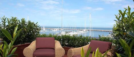 Una terraza con mobiliario de mimbre y vistas a un puerto deportivo con barcos.