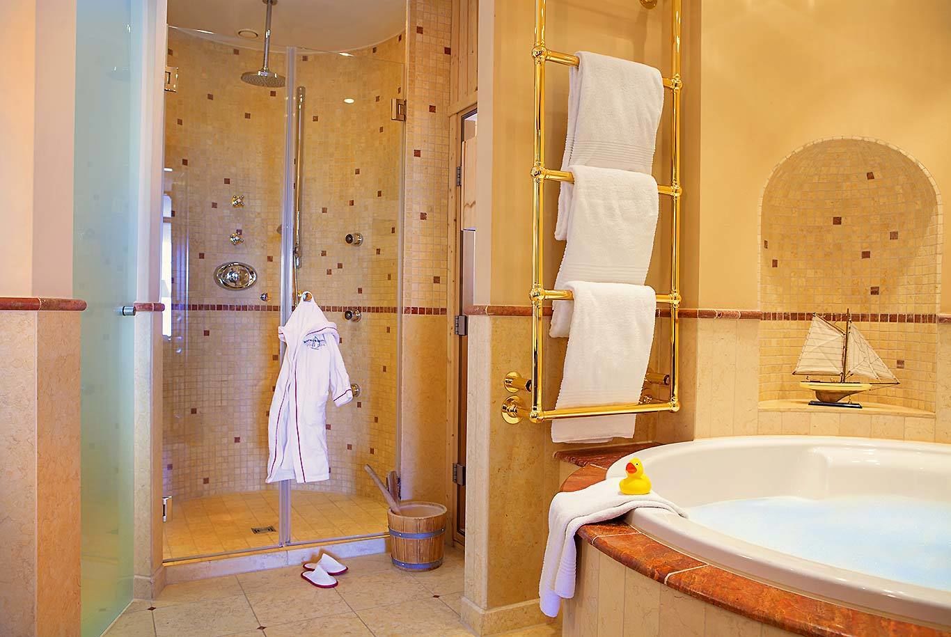 Ein Badezimmer mit begehbarer Dusche, einer Badewanne mit Schiffverzierung und einem Handtuchhalter mit mehreren Handtüchern.