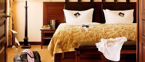 Una habitación de hotel con cama, mesita de noche, lámpara y una maleta.
