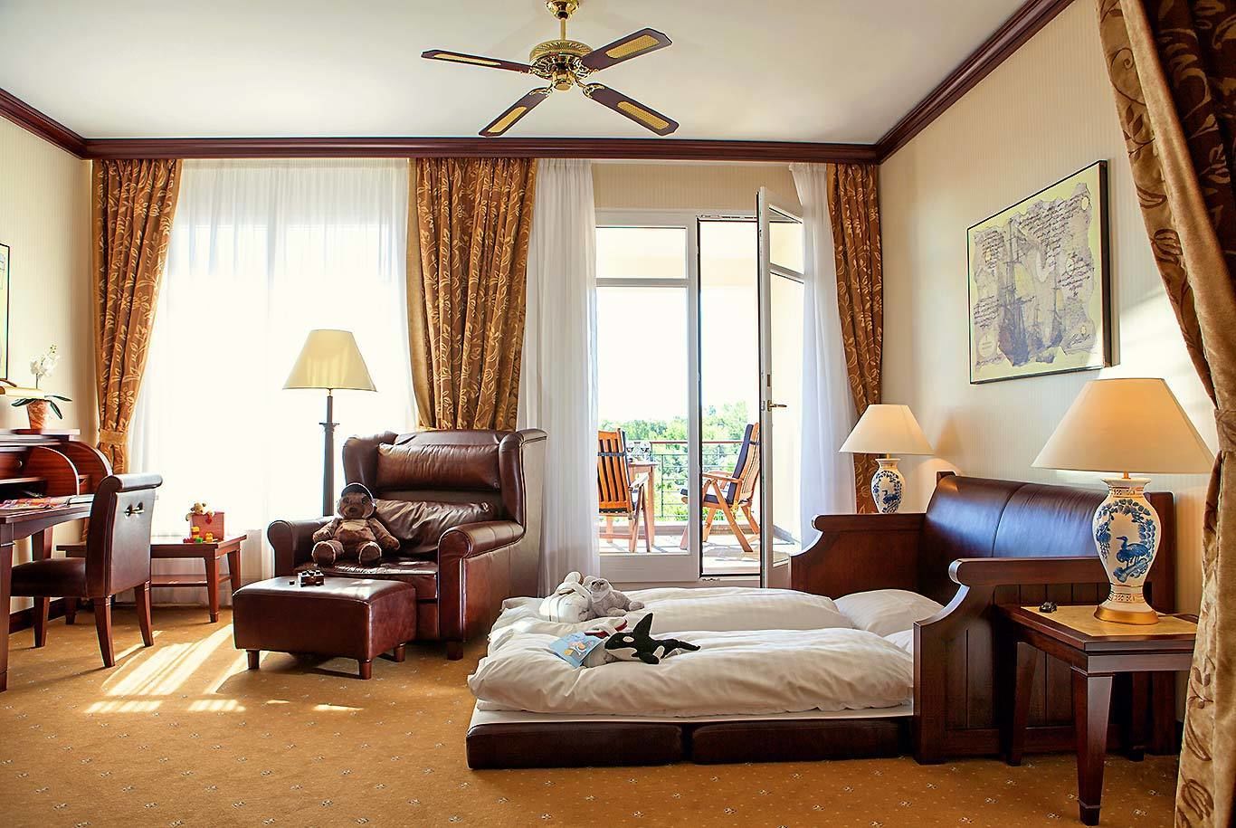 Habitación de hotel con cama, escritorio, silla, sofá, balcón con sillas y ventilador de techo.