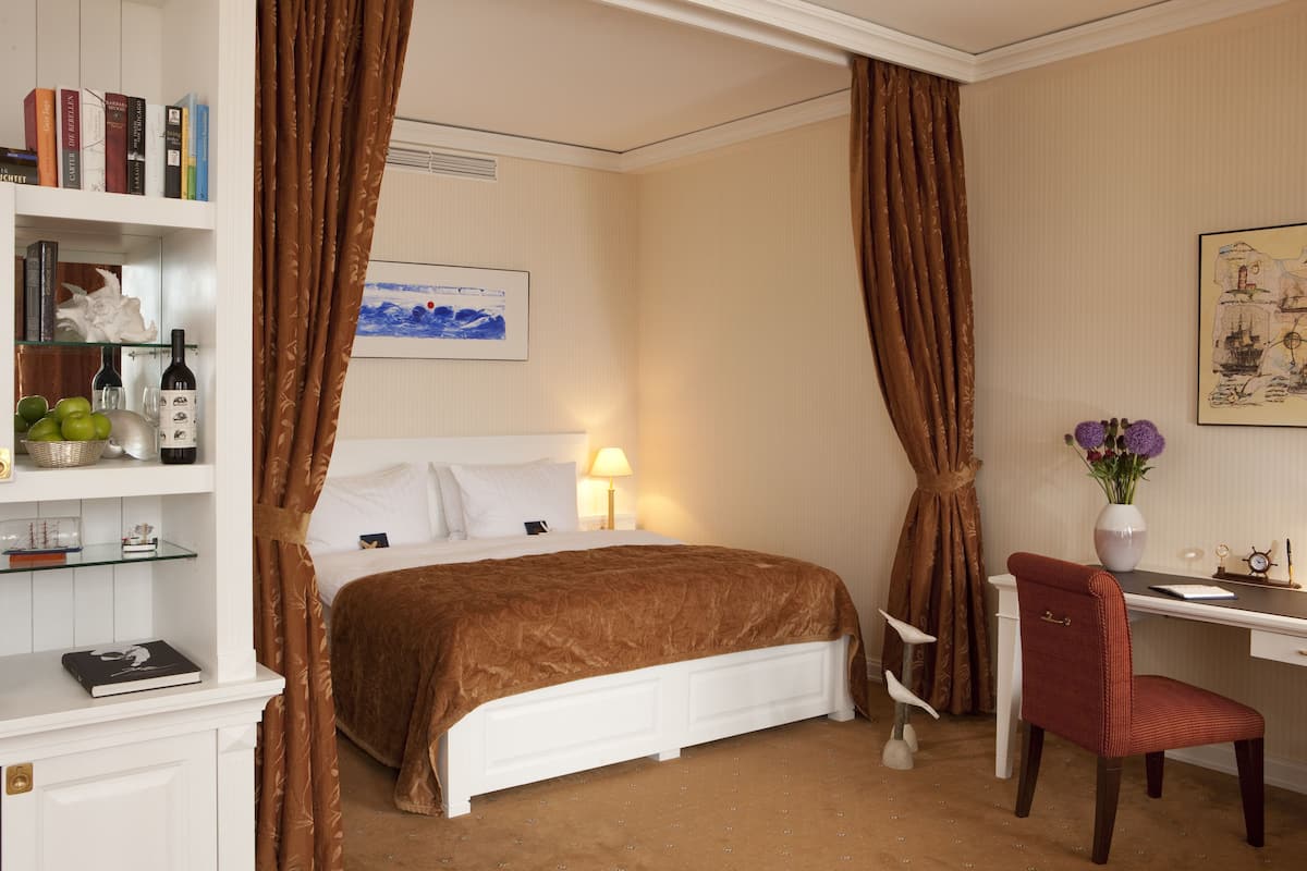 Ein Hotelzimmer mit Bett, Schreibtisch, Stuhl, Bücherregal und einem Gemälde an der Wand.