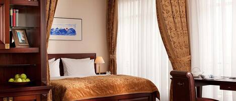 A hotel room with a wooden bed, a desk, a chair, a bookshelf, and a painting on the wall.