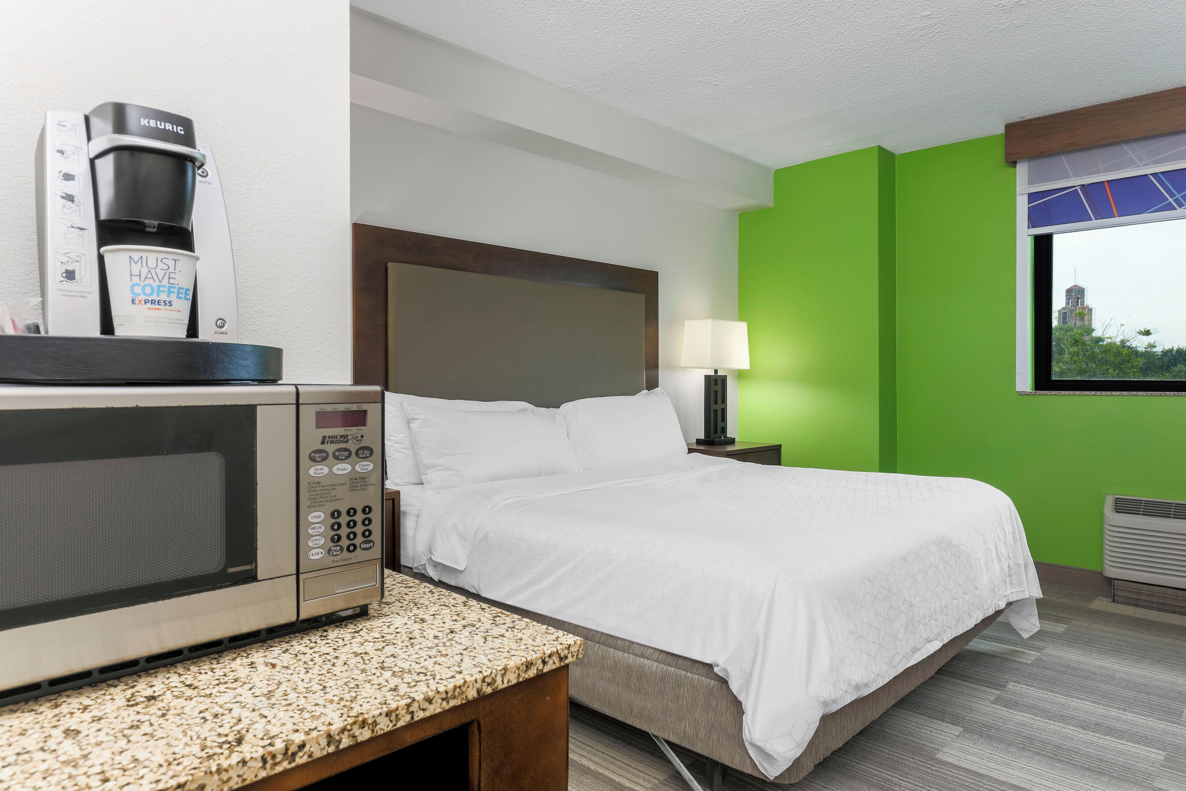 A hotel room with a bed, a coffee maker, a lamp, and a window with a view.