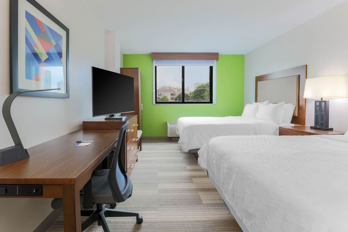 A hotel room with a desk, television, two beds, a window with a view, and a lamp.