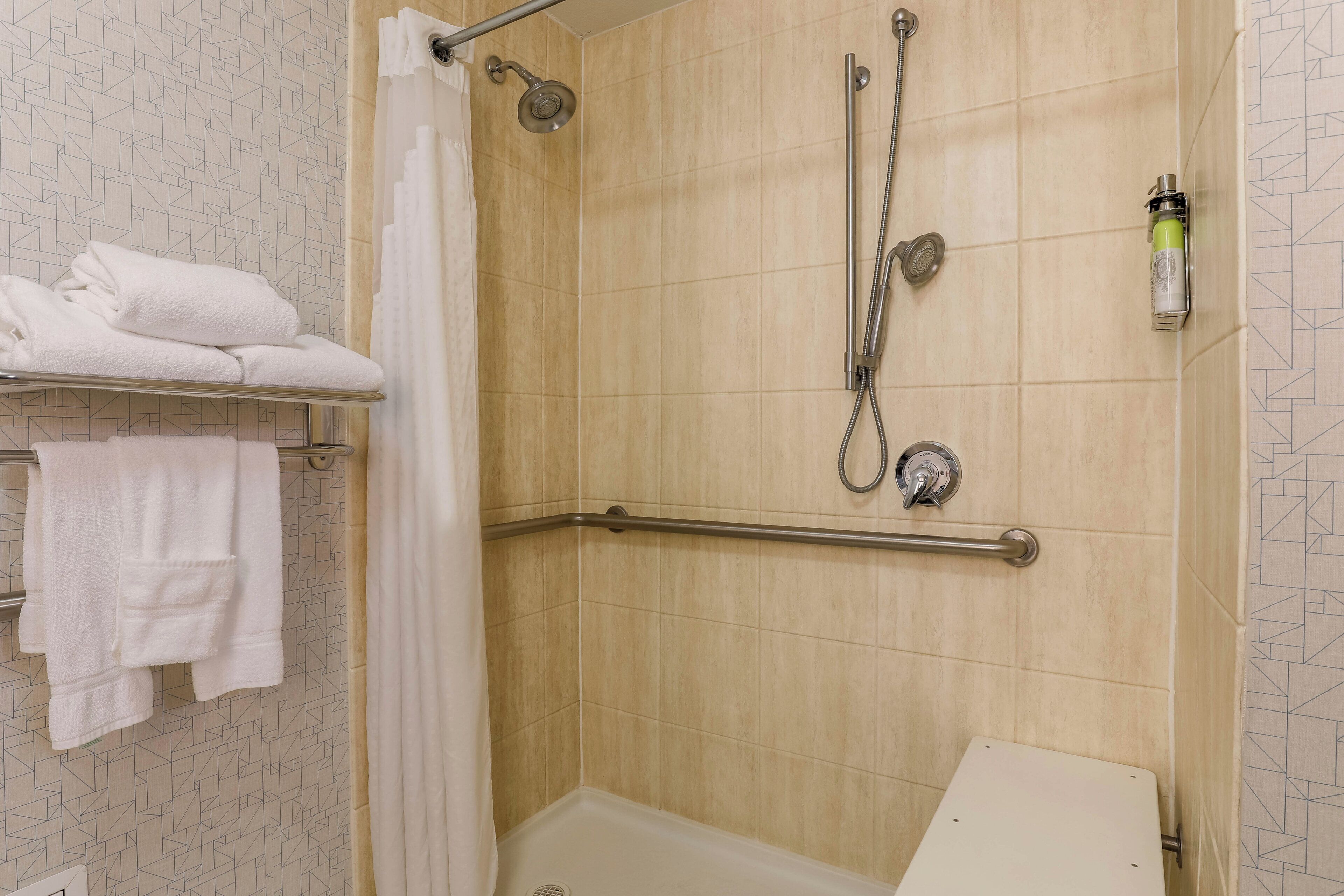 A shower area with a grab bar, a towel rack with folded towels, and a showerhead.