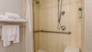 A shower area with a grab bar, a towel rack with folded towels, and a showerhead.