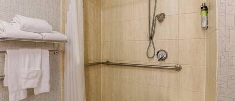 A shower area with a grab bar, a towel rack with folded towels, and a showerhead.