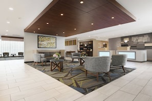 A hotel lobby with a modern design, featuring a seating area with chairs and a sofa, a reception desk, and a decorative wall with a geometric pattern. - Holiday Inn Express & Suites Fort Worth Downtown by IHG (Fort Worth)