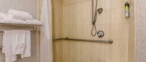 A shower area with a grab bar, a towel rack with folded towels, and a showerhead.