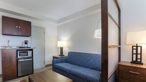 Una habitación de hotel compacta con kitchenette, un sofá, una mesa de madera y una lámpara.