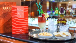 Zona de bar con carta de cócteles, una bebida con pajita y una botella de Chivas Regal sobre una bandeja con queso y galletas.