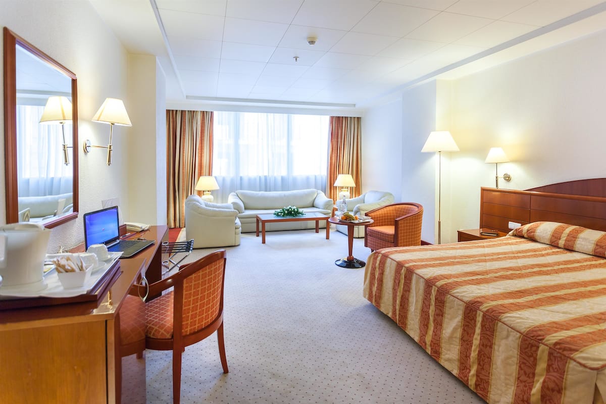 Habitación de hotel con cama, escritorio con computadora portátil, silla, sofá y pequeña mesa con lámpara.