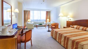 Habitación de hotel con cama, escritorio con computadora portátil, silla, sofá y pequeña mesa con lámpara.