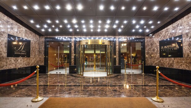 Entrada de hotel con piso de mármol, puerta giratoria y una barrera de cuerda roja.