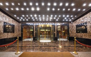Entrada de hotel con piso de mármol, puerta giratoria y una barrera de cuerda roja.