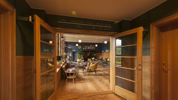 Un interior espacioso con un suelo de parqué tipo espiga, puertas de madera abiertas que dan a un comedor con mesas y sillas, y un menú visible en la pared.
