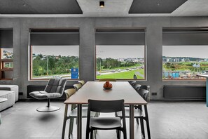 Una sala de reuniones moderna con una gran mesa, sillas cómodas y ventanas amplias que ofrecen vistas a un paisaje urbano y una autopista.
