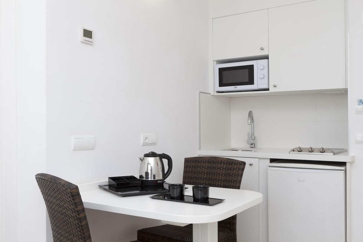 Una kitchenette compacta con microondas, hervidor y refrigerador pequeño.