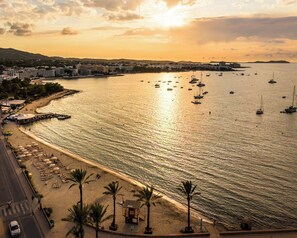 Vista costera con playa, barcos y un paisaje urbano al fondo.