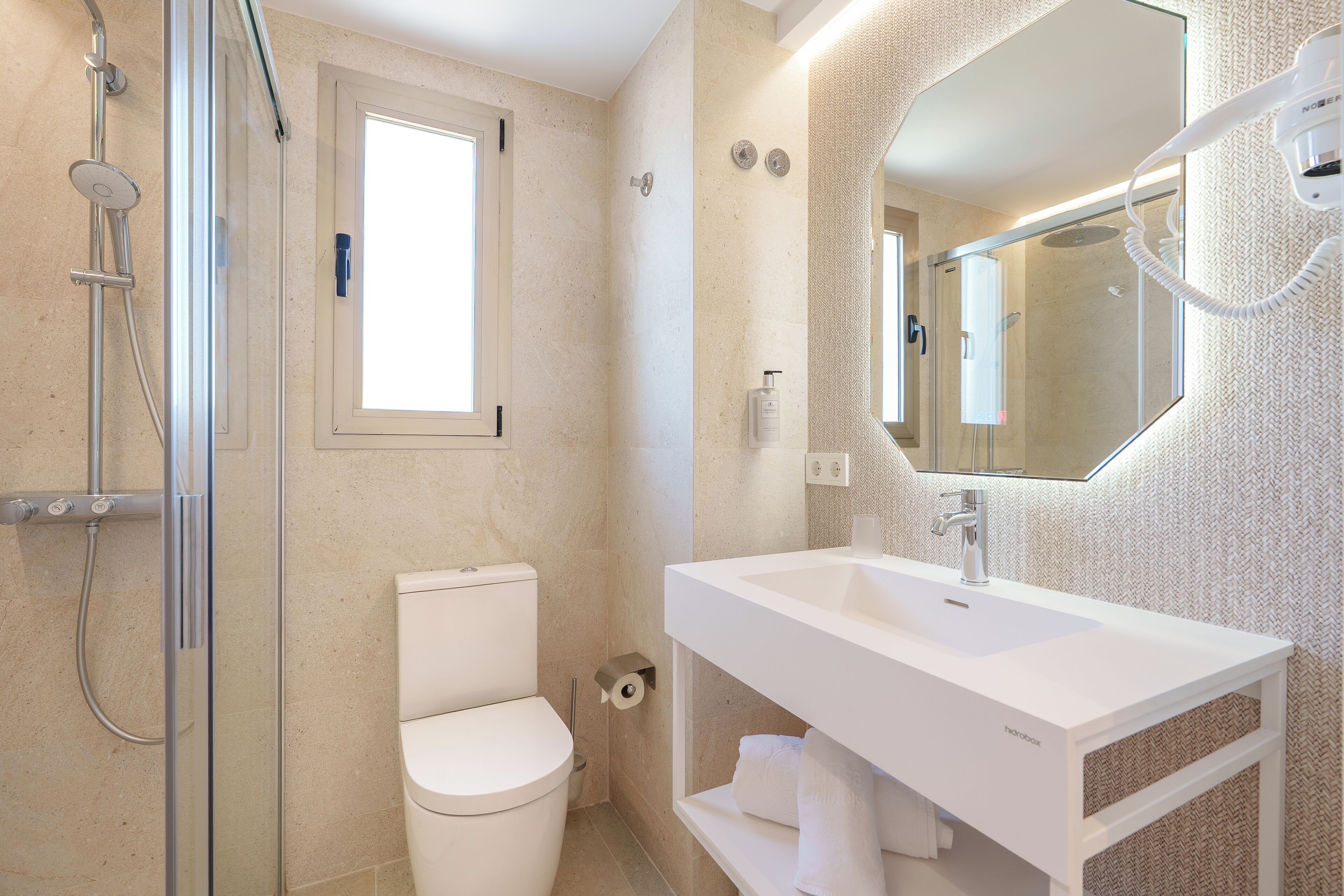 A modern bathroom with a glass shower enclosure, a toilet, and a white sink with a mirror above it.