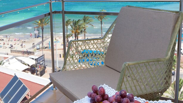 Een balkon met uitzicht op het strand en de oceaan, een stoel en een schaal fruit.