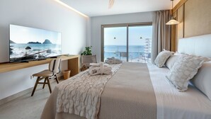 Een moderne hotelkamer met een groot bed, een televisie aan de muur, een bureau met stoel en uitzicht op zee.
