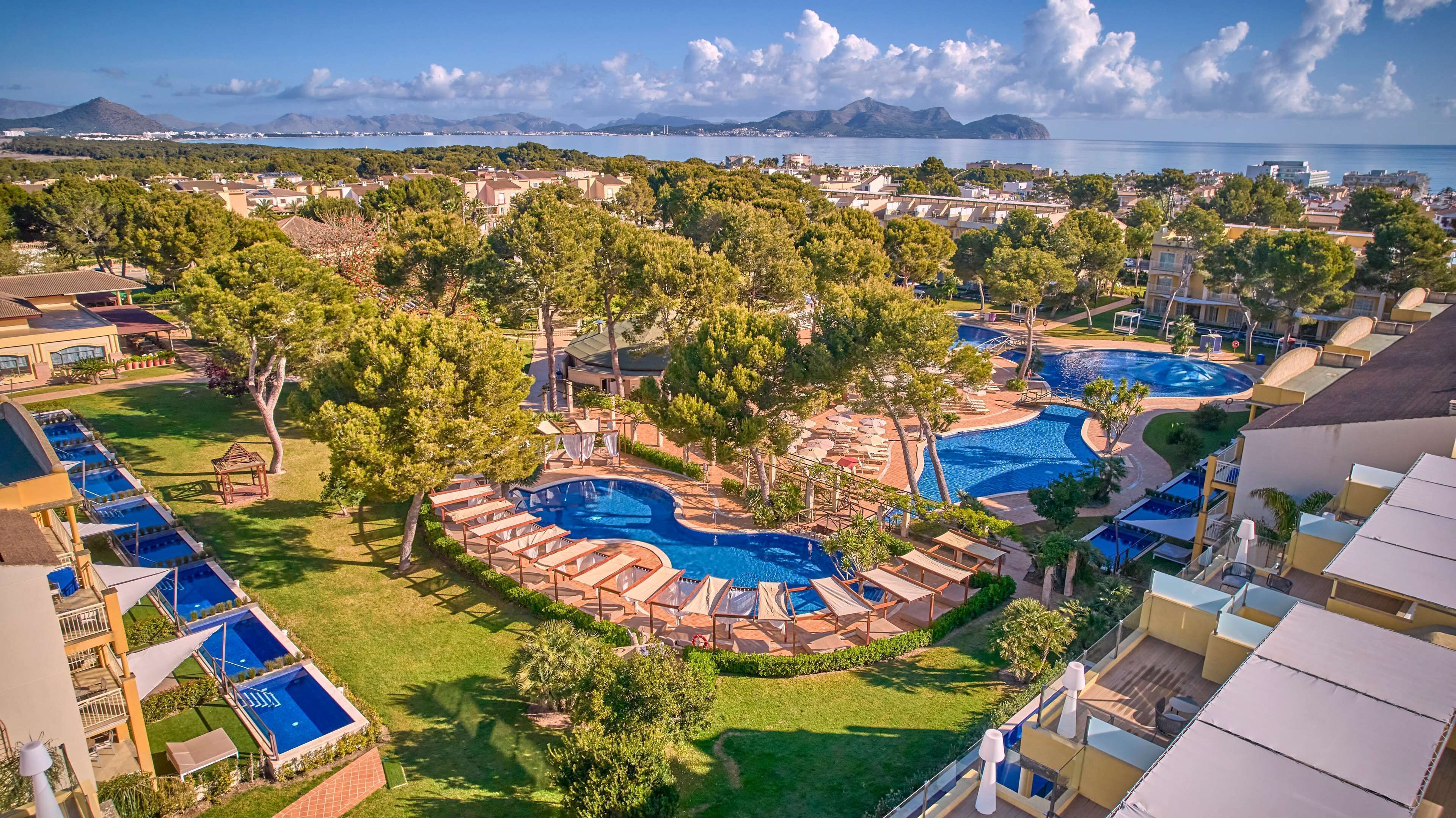 A resort with multiple swimming pools, lush greenery, and a view of the sea and mountains.