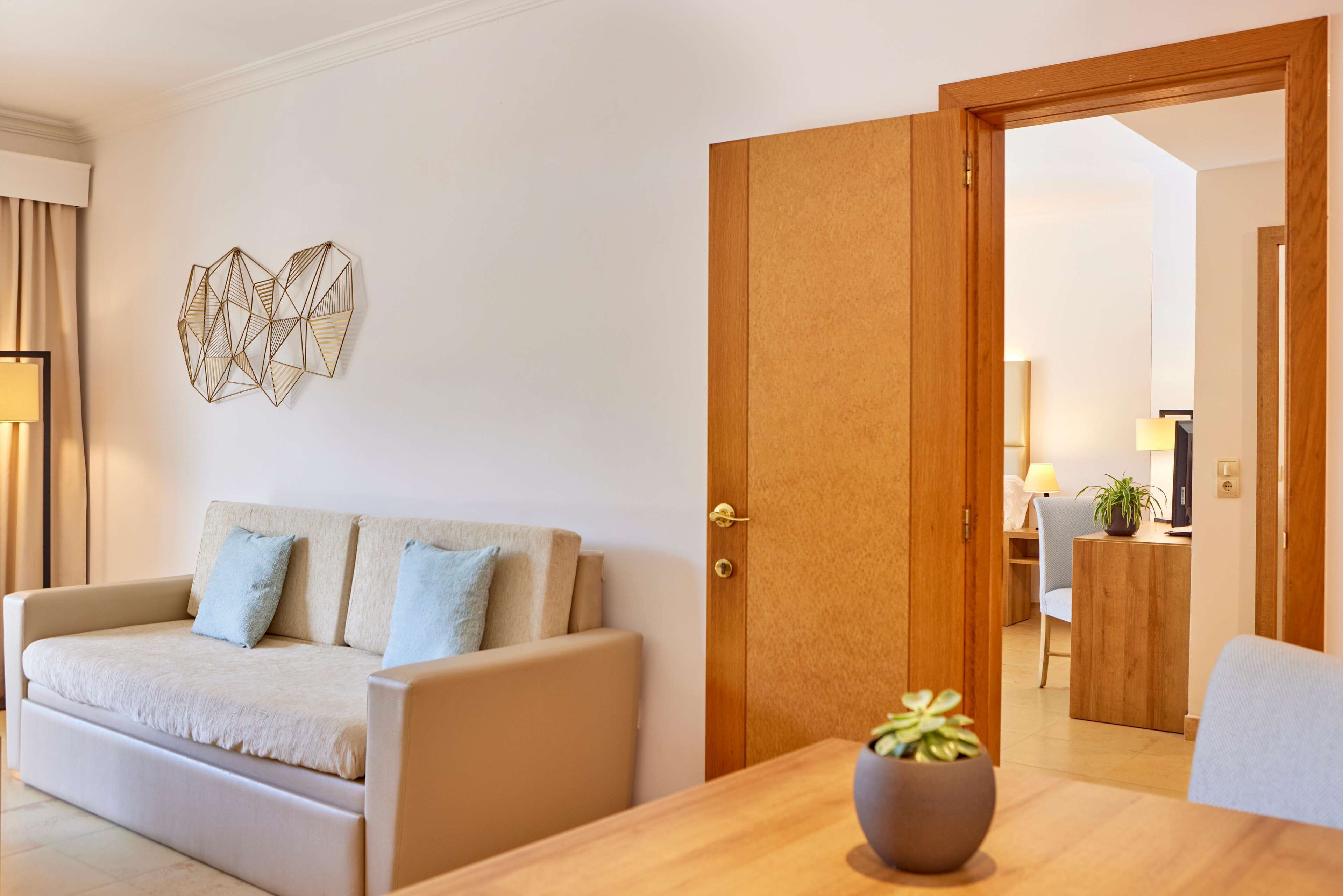 A modern living room with a sofa, a wooden door, and a dining table with a potted plant.
