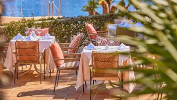 Outdoor dining tables with wicker chairs and white tablecloths, set against a poolside backdrop.