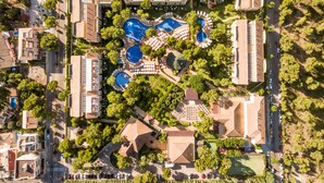 An aerial view of a resort with multiple swimming pools, guest villas, and lush greenery.