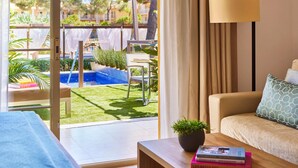 A modern living room with a sofa, a coffee table with books, a lamp, and a view of a pool and garden.