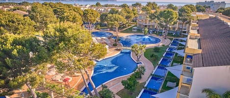 Een resort met meerdere zwembaden, weelderige begroeiing en uitzicht op de zee.