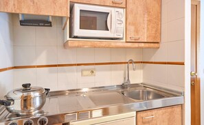 A kitchen with a microwave, stove, sink, and wooden cabinets. - Zafiro Mallorca (Santa Margalida)