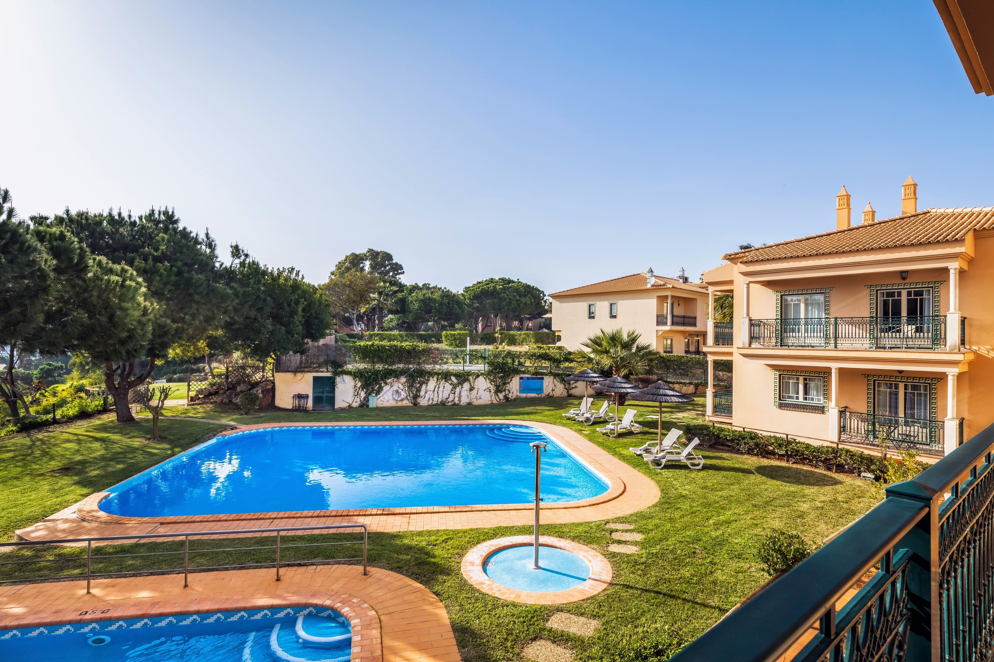 A swimming pool with a tiled deck, surrounded by a well-maintained lawn and a building with balconies.