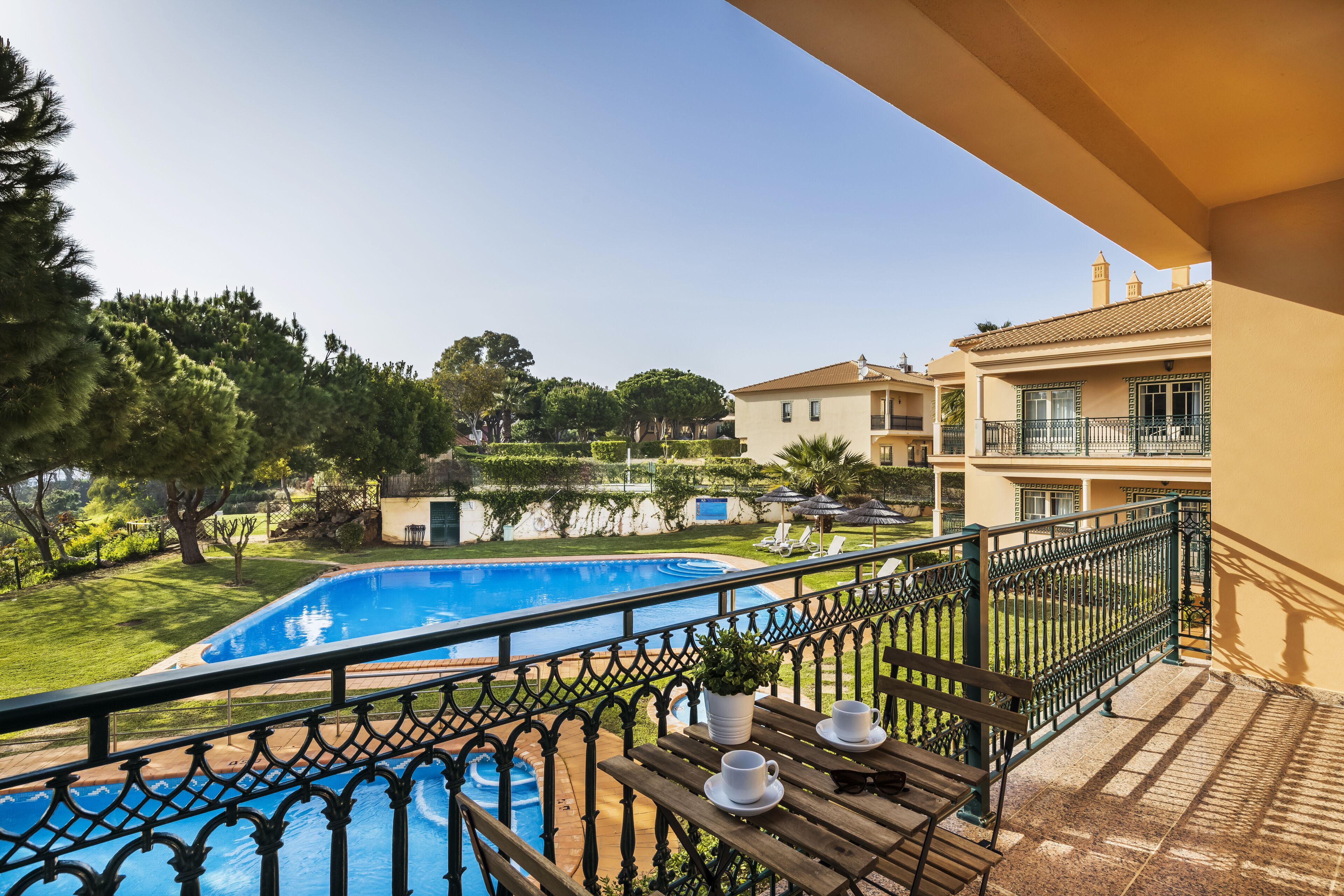 Un balcó amb vista a una piscina, una taula de fusta amb tasses i una barana.