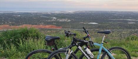Two bicycles parked on a grassy hill overlooking a valley with a distant view of a city and a large open area.