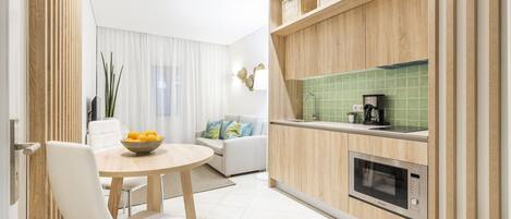 Una cocina moderna con armarios de madera, microondas integrado y comedor con mesa redonda y sillas blancas.