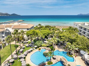 Un resort con una gran piscina, palmeras y vista al océano.