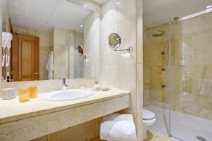 A modern bathroom with a marble sink, a large mirror, a glass-enclosed shower, and a wooden cabinet.