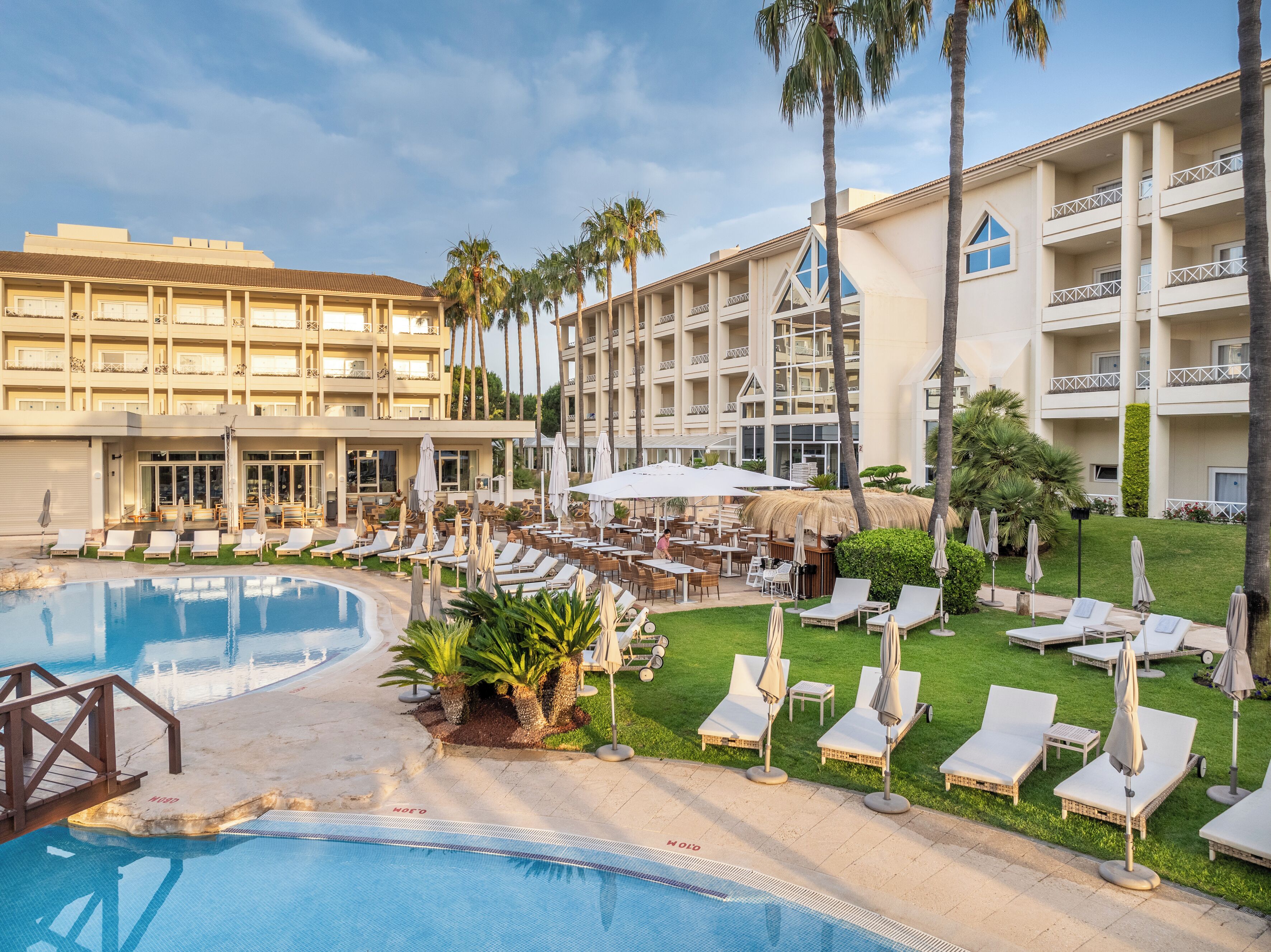 Ein Hotel mit Poolbereich, Außenbereich und Palmen.