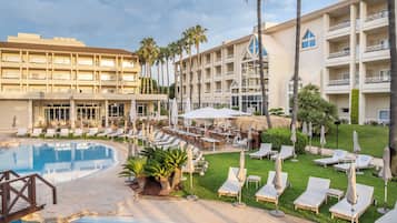 Un hotel con piscina, mobiliario exterior y palmeras.