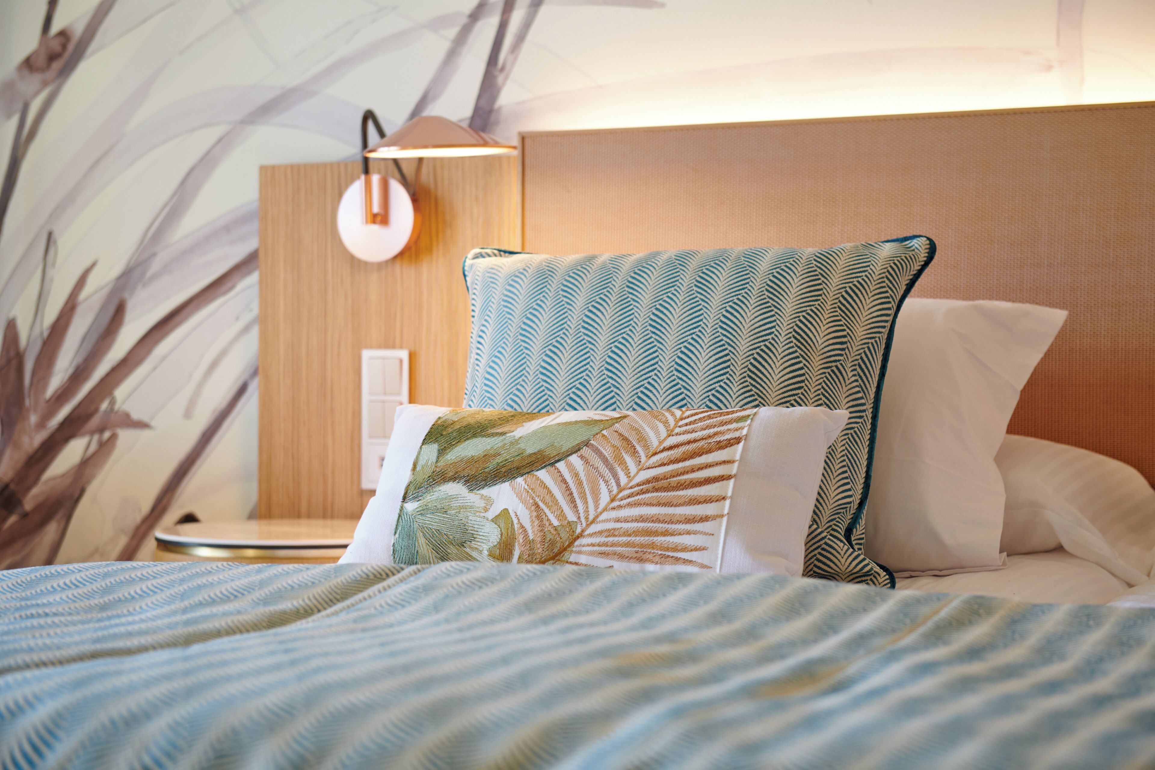 A neatly made bed with patterned bedding, a wall-mounted lamp, and a wooden headboard.