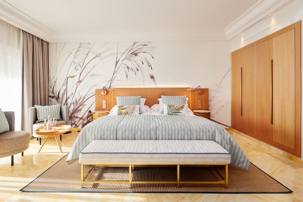 Ein modernes Hotelzimmer mit einem großen Bett, einer Couch, einem kleinen Tisch und einem großen Fenster mit Vorhängen.